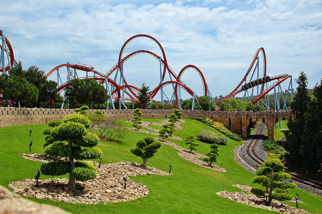 A red roller coaster winding through landscaped park grounds